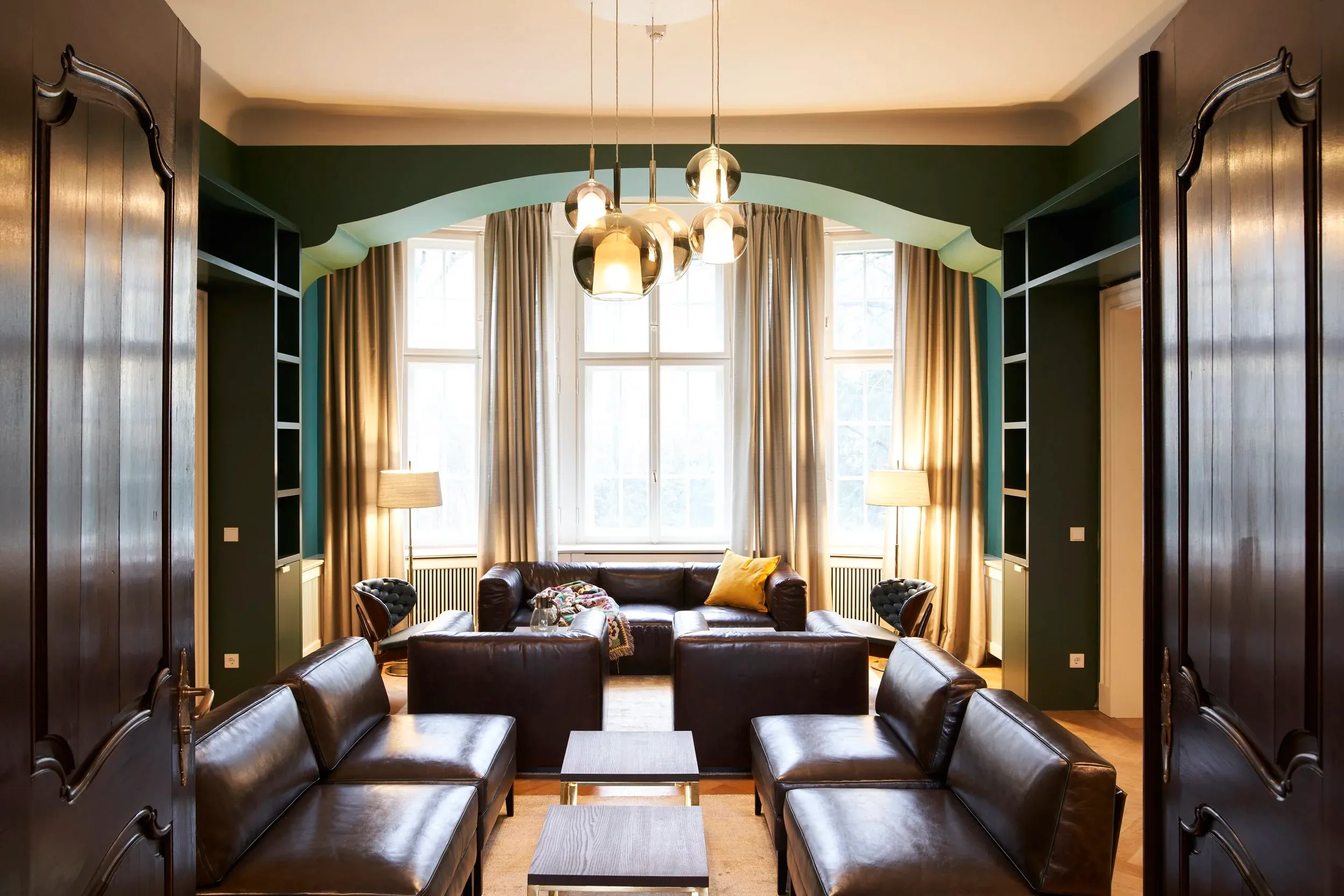 Symmetrischer Blick durch die Flügeltür in den grünen Salon mit Ledersofas