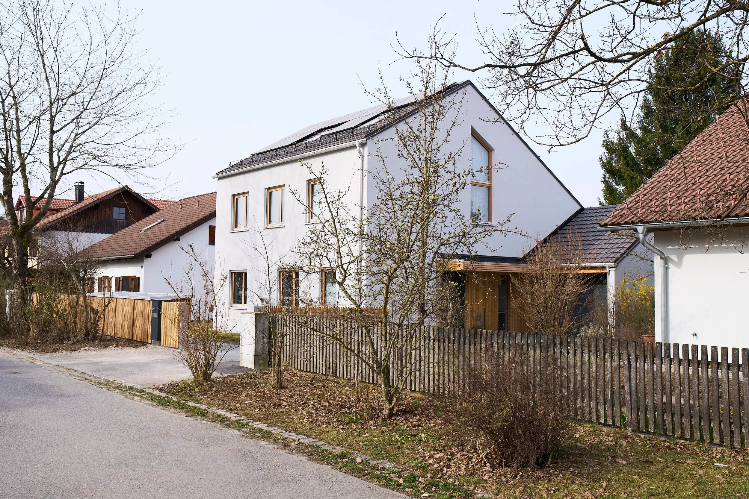 Straßenansicht mit Satteldach, Photovoltaikanlage und Holzlattenzaun