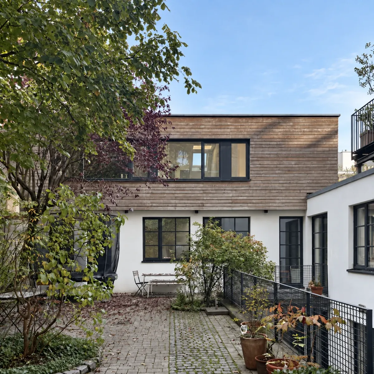 Begrünter Innenhof mit Holzaufstockung, dunklen Fenstern und Sitzbank