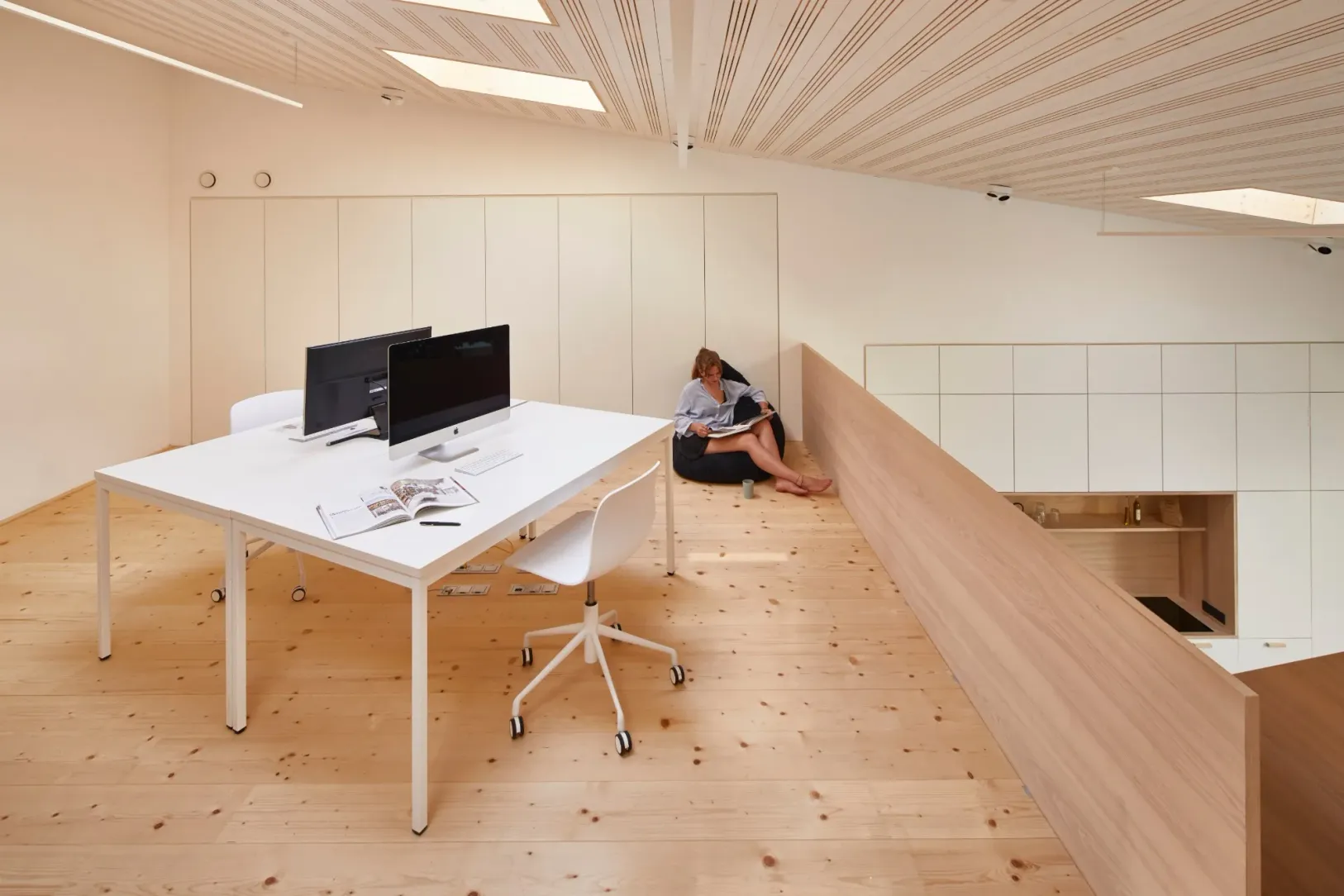 Galerie mit weißen Arbeitstischen, Sitzsack und Blick über die Holzbrüstung in die Küche