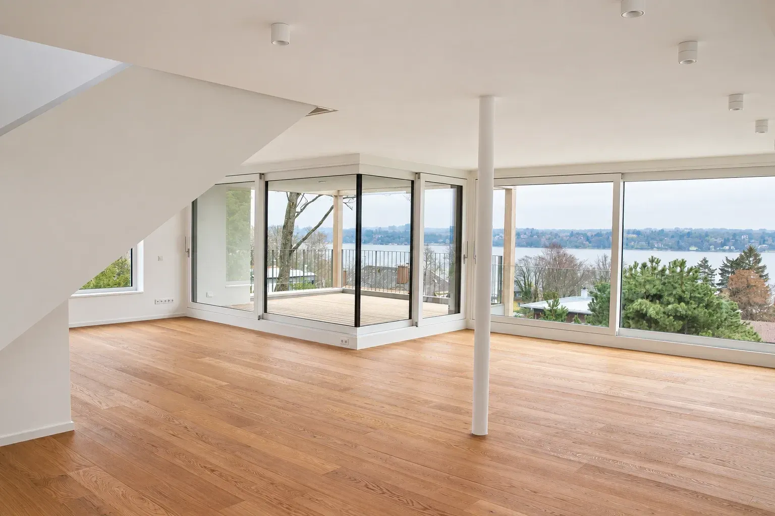 Heller Wohnraum mit Holzboden, weißer Stütze und Eckverglasung zur Terrasse, Blick auf den See