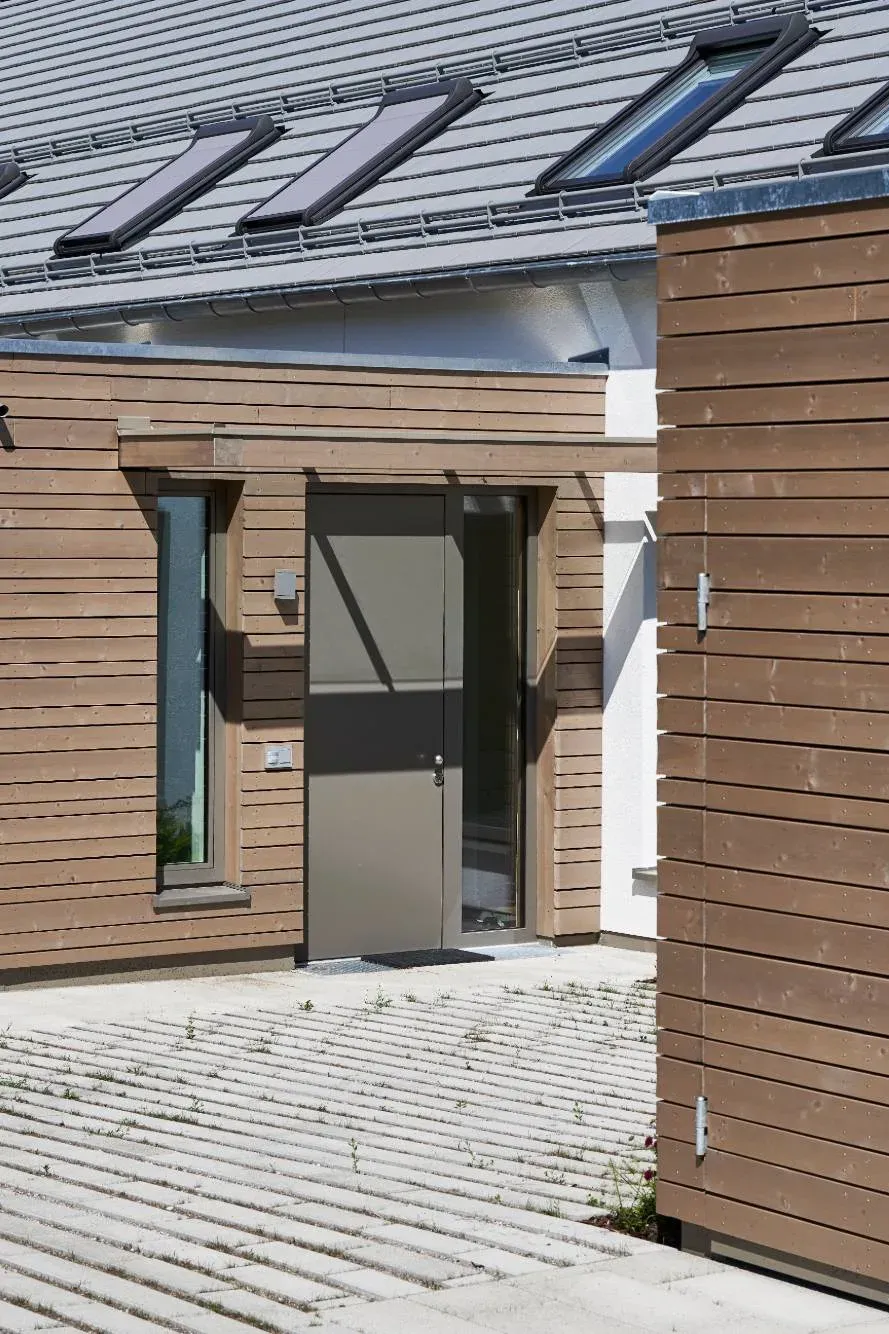 Hauseingang mit grauer Tür und schmalem Fenster in der Holzfassade