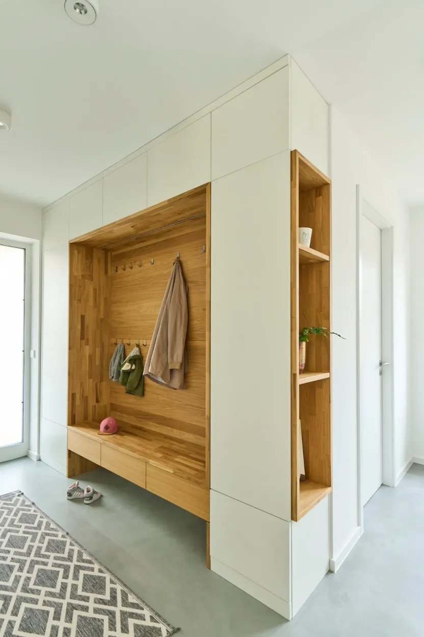 Einbaugarderobe mit weißen Schrankfronten, Holznische mit Haken und Sitzbank, daneben ein offenes Holzregal
