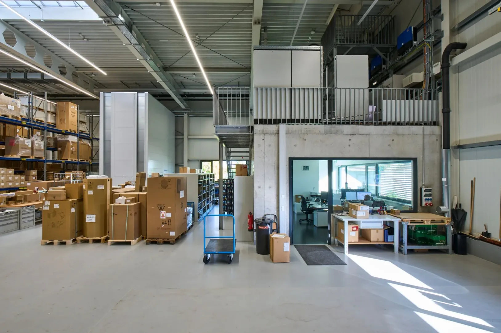 Lagerhalle mit Stahltreppe und Galerie, darunter ein verglastes Büro in der Sichtbetonwand
