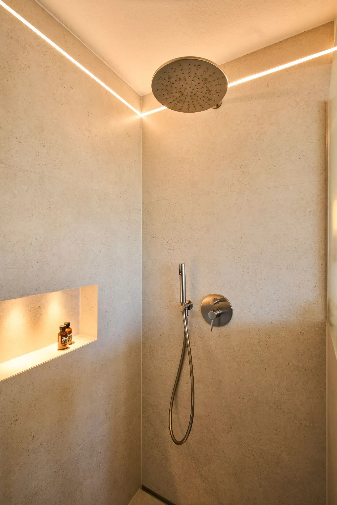 Dusche mit großformatigen Steinplatten, Regendusche, beleuchteter Wandnische und Lichtfuge an der Decke